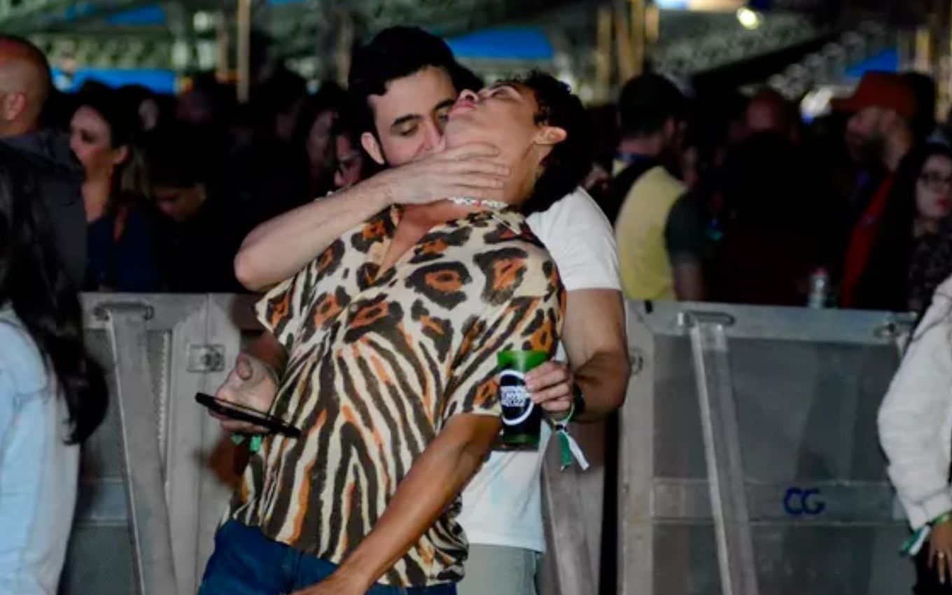 O ator Silvero Pereira é beijado no pescoço por um homem barbudo durante um show