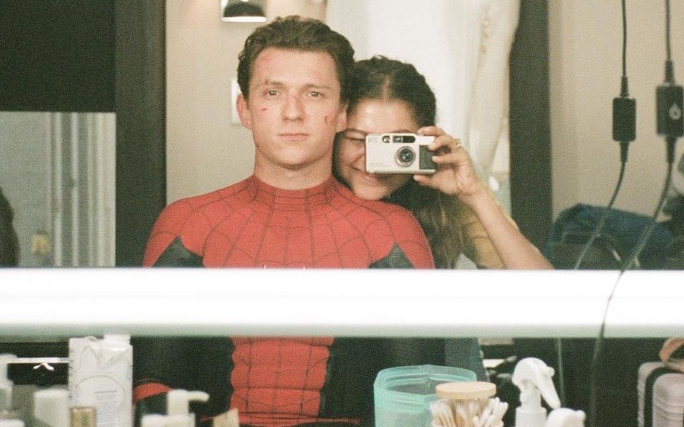 Tom Holland vestido de Homem-Aranha, e Zendaya tirando foto no espelho